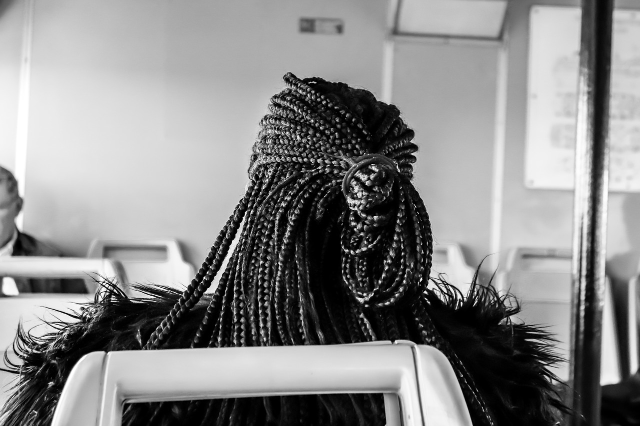 Photo en noir et blanc d'une personne assise de dos. Elle porte des tresses fines et longues en partie attachées.